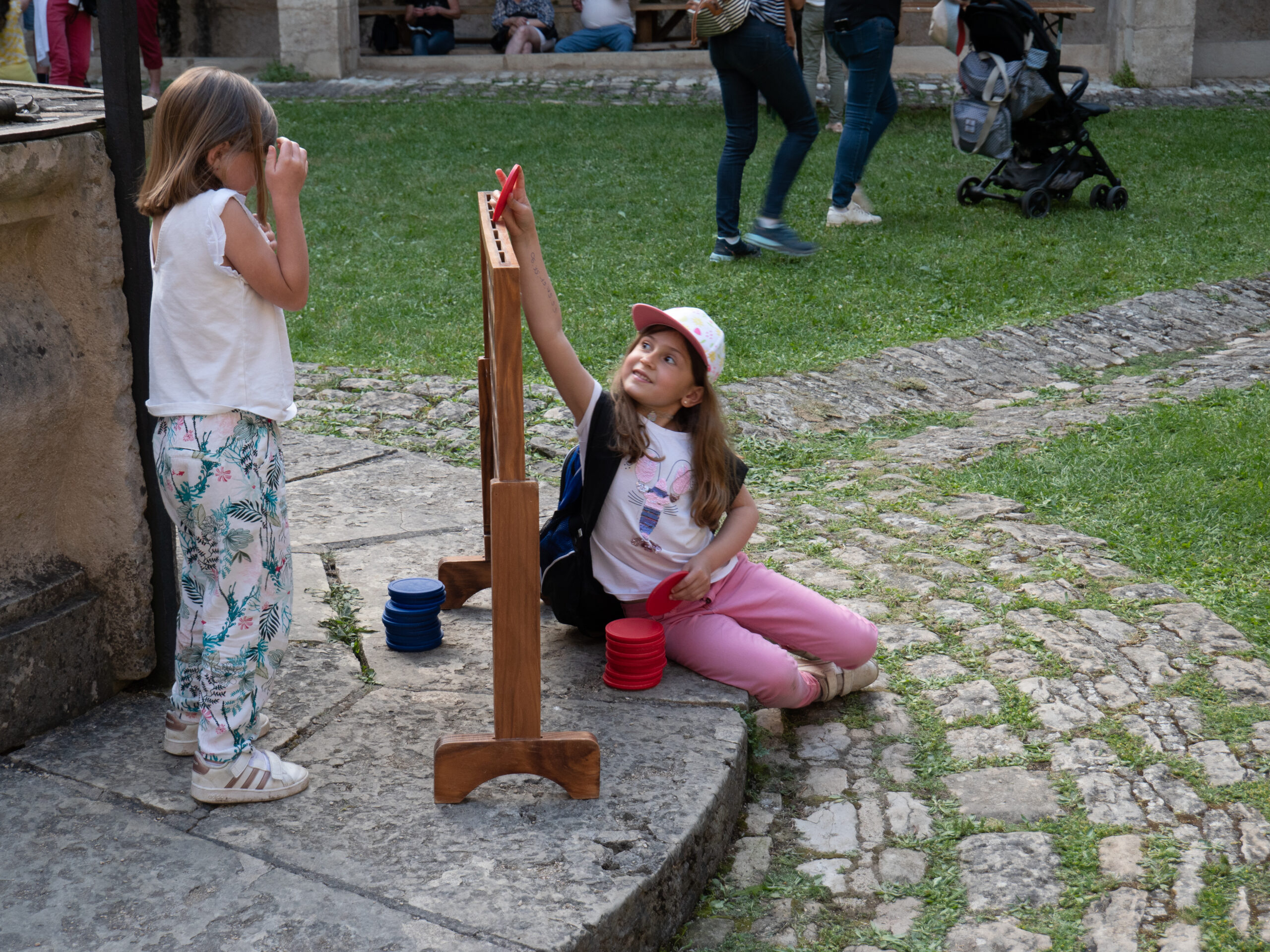 Deux fillette jouent à une puissance quatre géant, près d'une fontaine aux contours herbacés