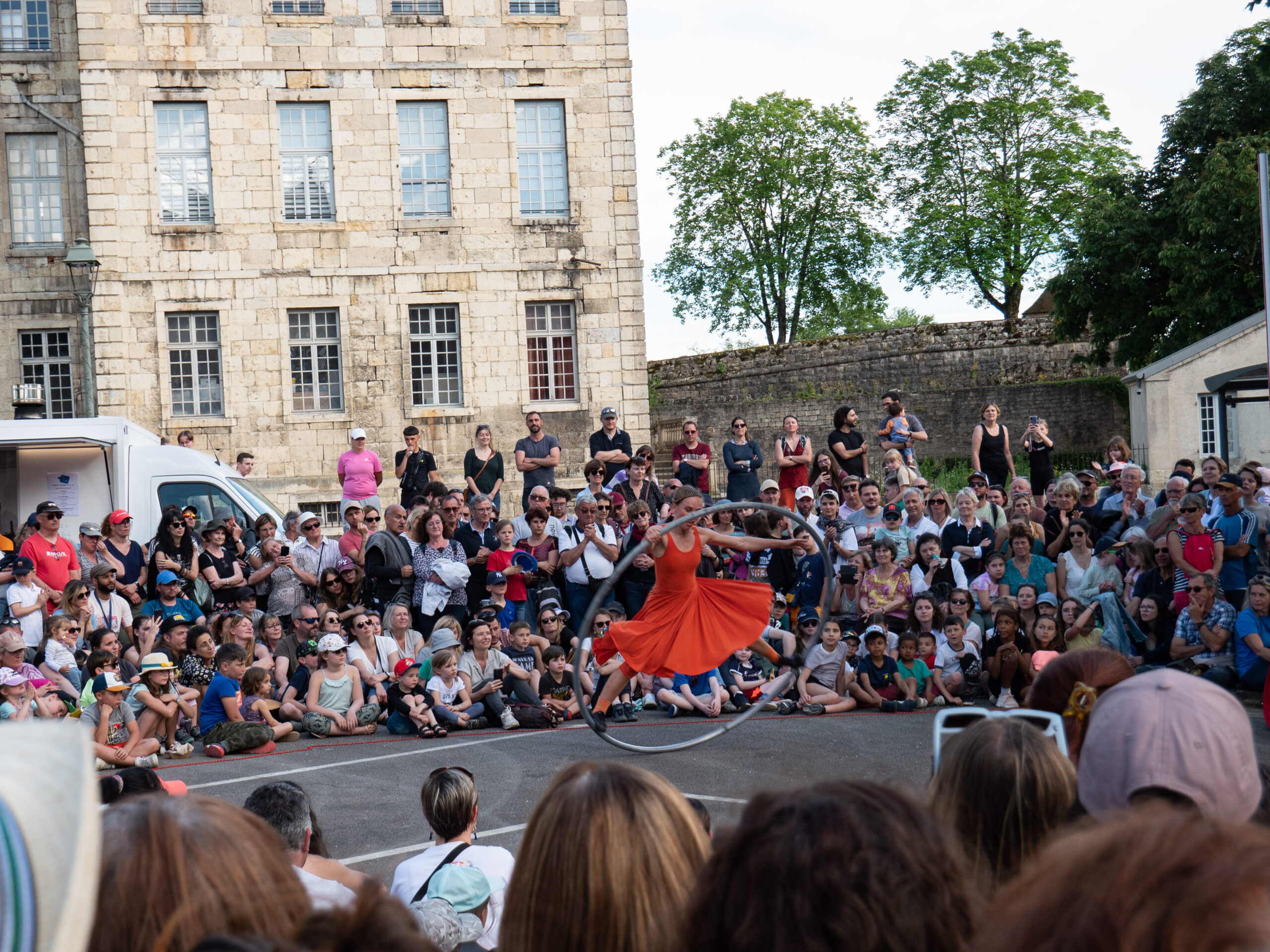 Une femme acrobate en robe rouge qui fait un numéro sur un grand cerceau, entourée d'une foule composée de nombreux enfants