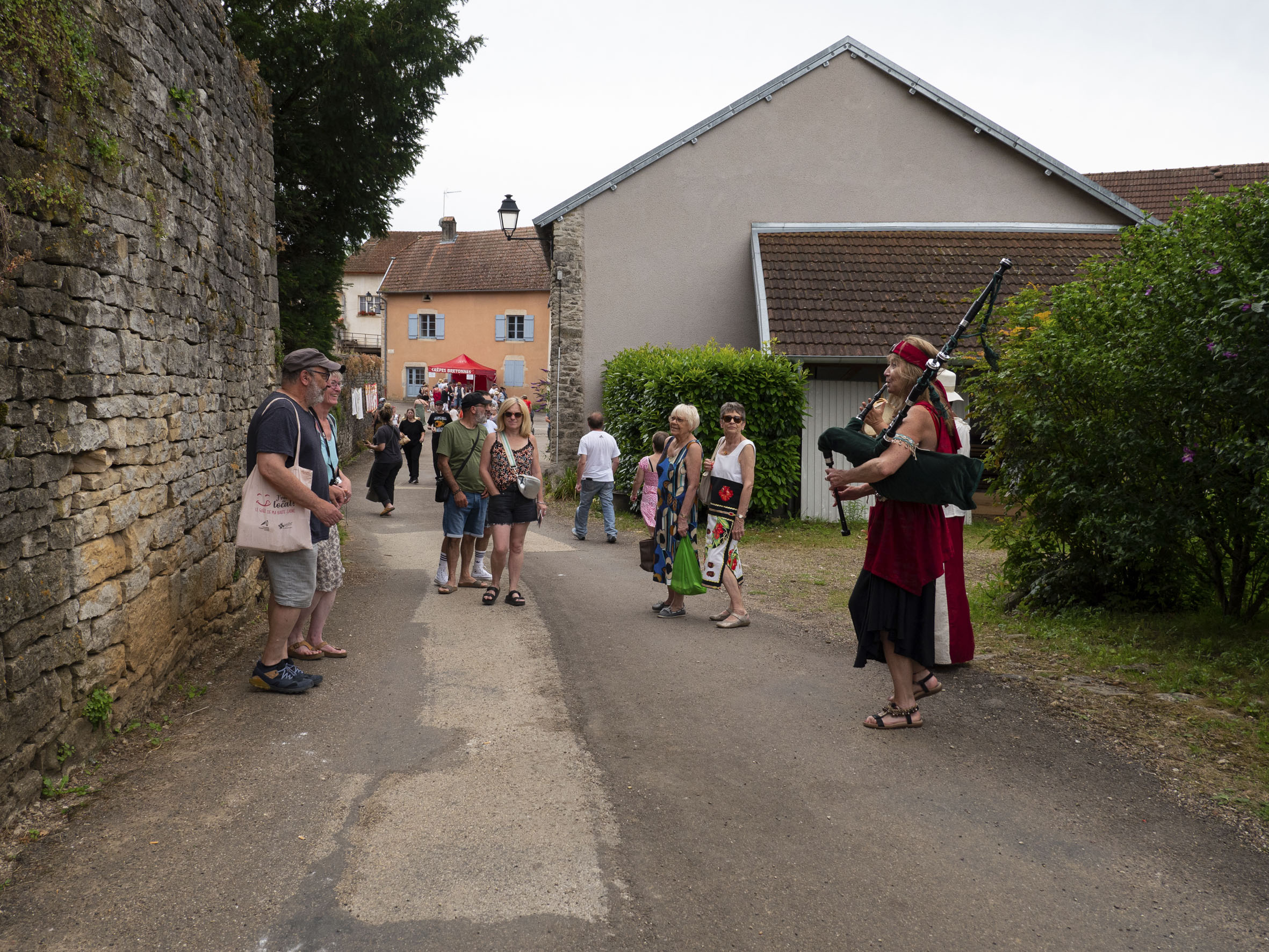 quelques personnes passant à côté de musiciens de costumes, dont une femme à la cornemuse