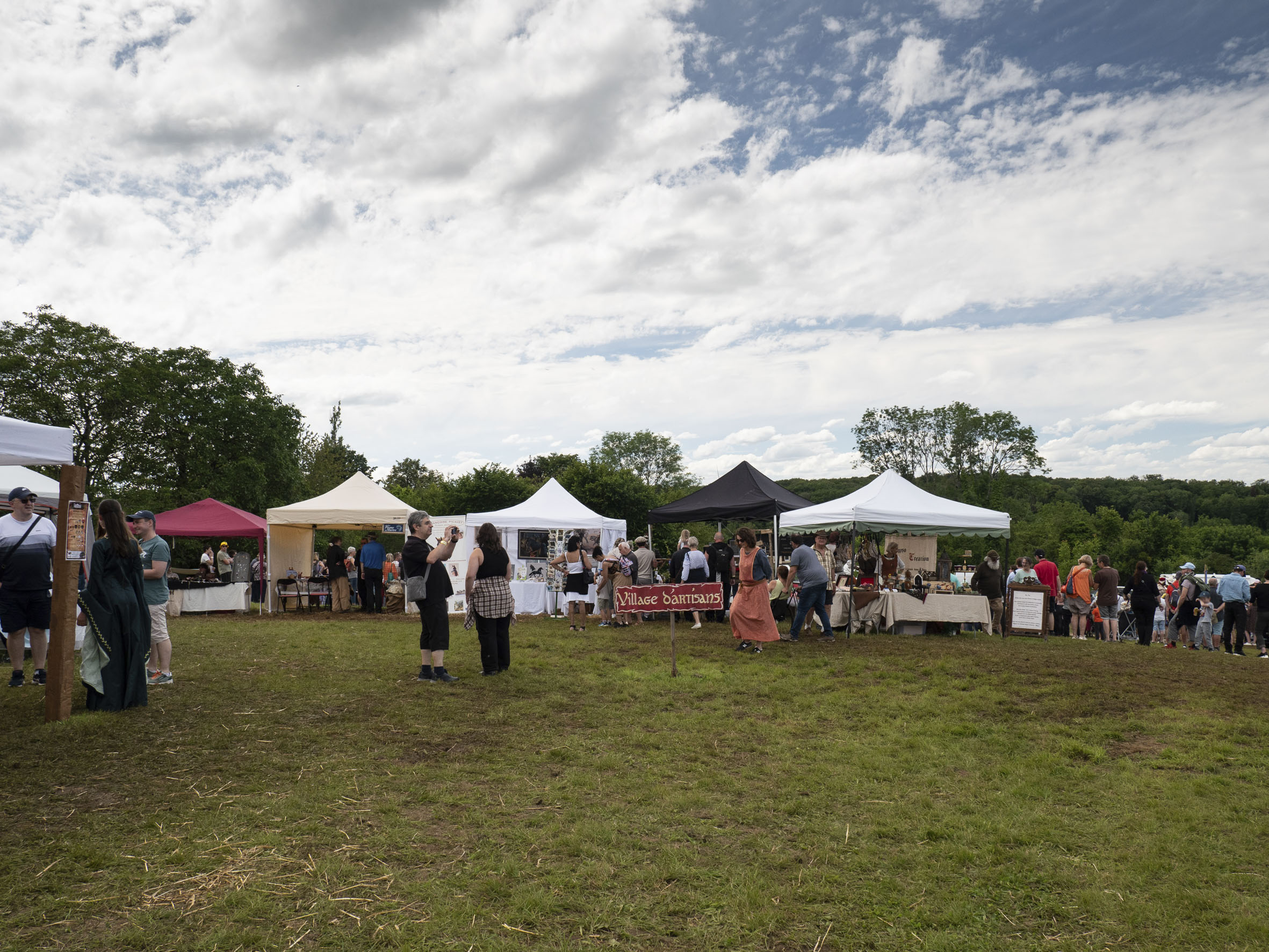 photo du village d'artisans monté dans l'herbe, avec des visiteurs, dont certains en costume