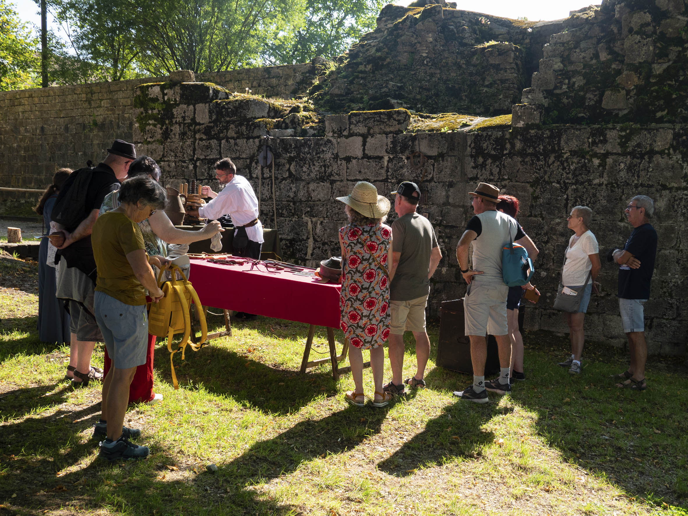 groupe de personnes attroupées autour d'un artisan travaillant le métal, au pied d'une fortification en pierre