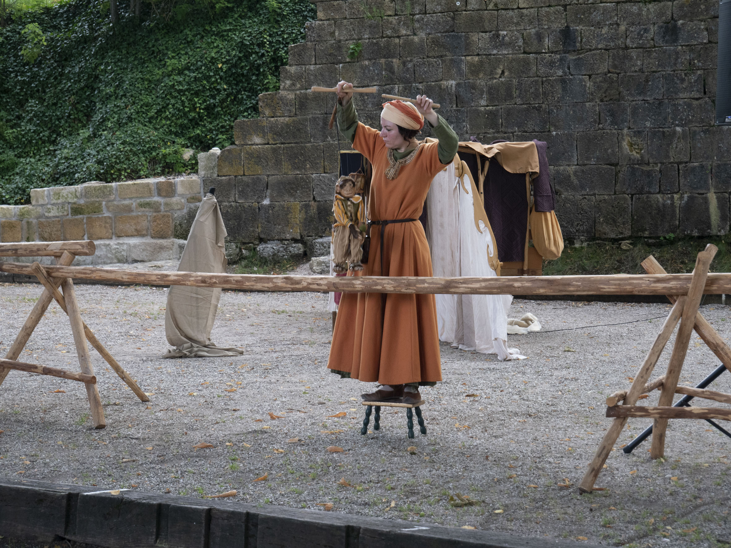 spectacle de marionnettes donné par une femme en costume, dans une cour au pied d'un rempart en pierre