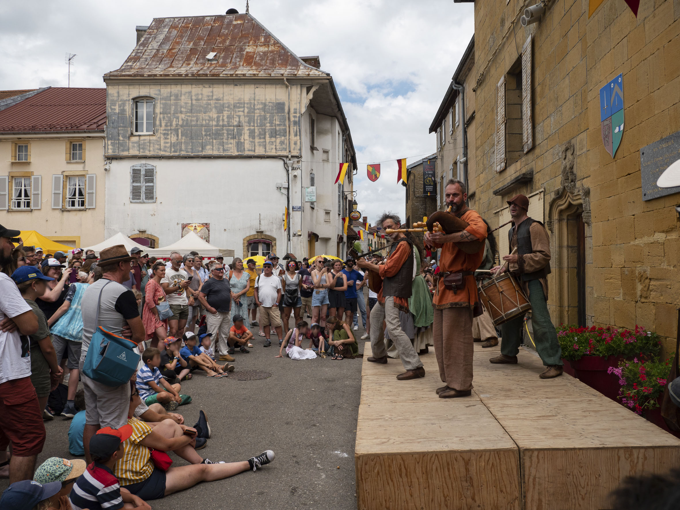 fanfare (cornemuse, guitare, tambour) devant une importante foule, dont de nombreux enfants assis par terre