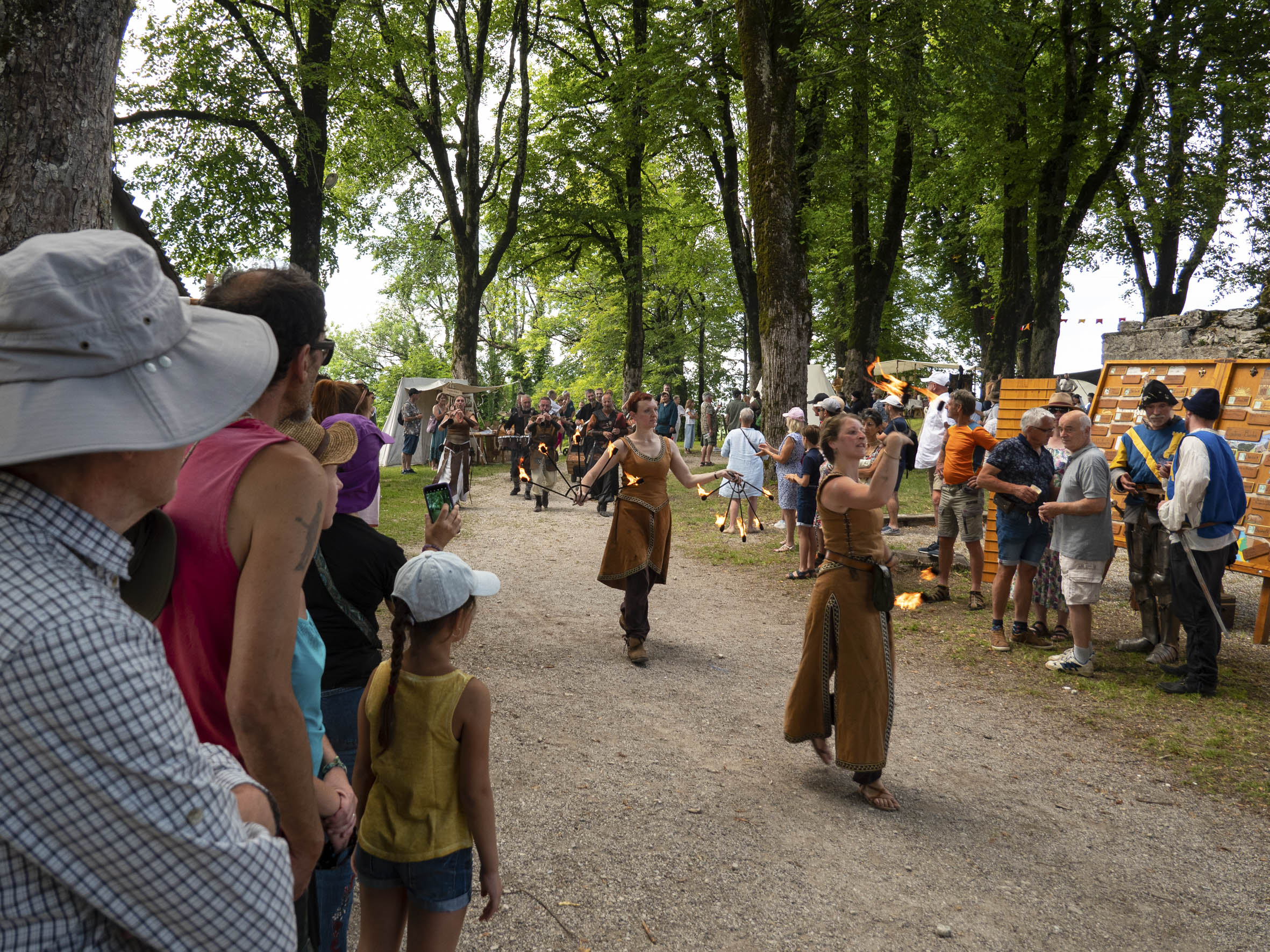 troupe d'artistes jouant avec le feu sur un chemin entre les arbres, sous les yeux de la foule