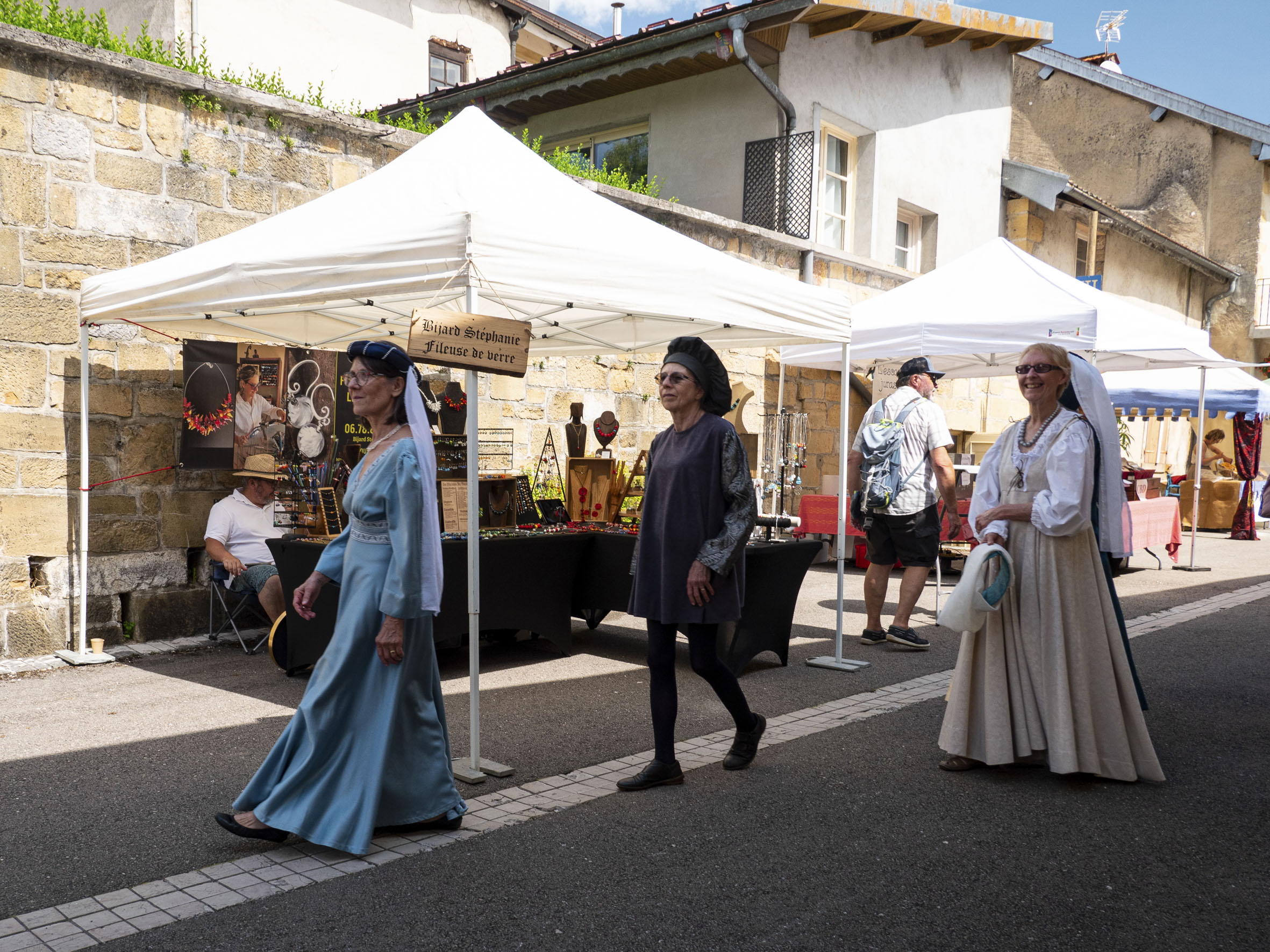 trois femmes en costume de dames de la cour, qui passent le long d'une allée de stands