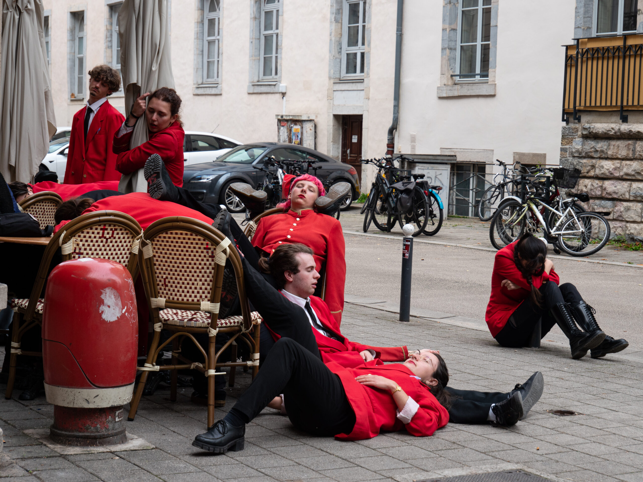 Les personnes vêtues de rouge installées à une terrasse, semblant s'être endormies sur les chaises, les tables, le sol, les poteaux du trottoir, sous un angle différent