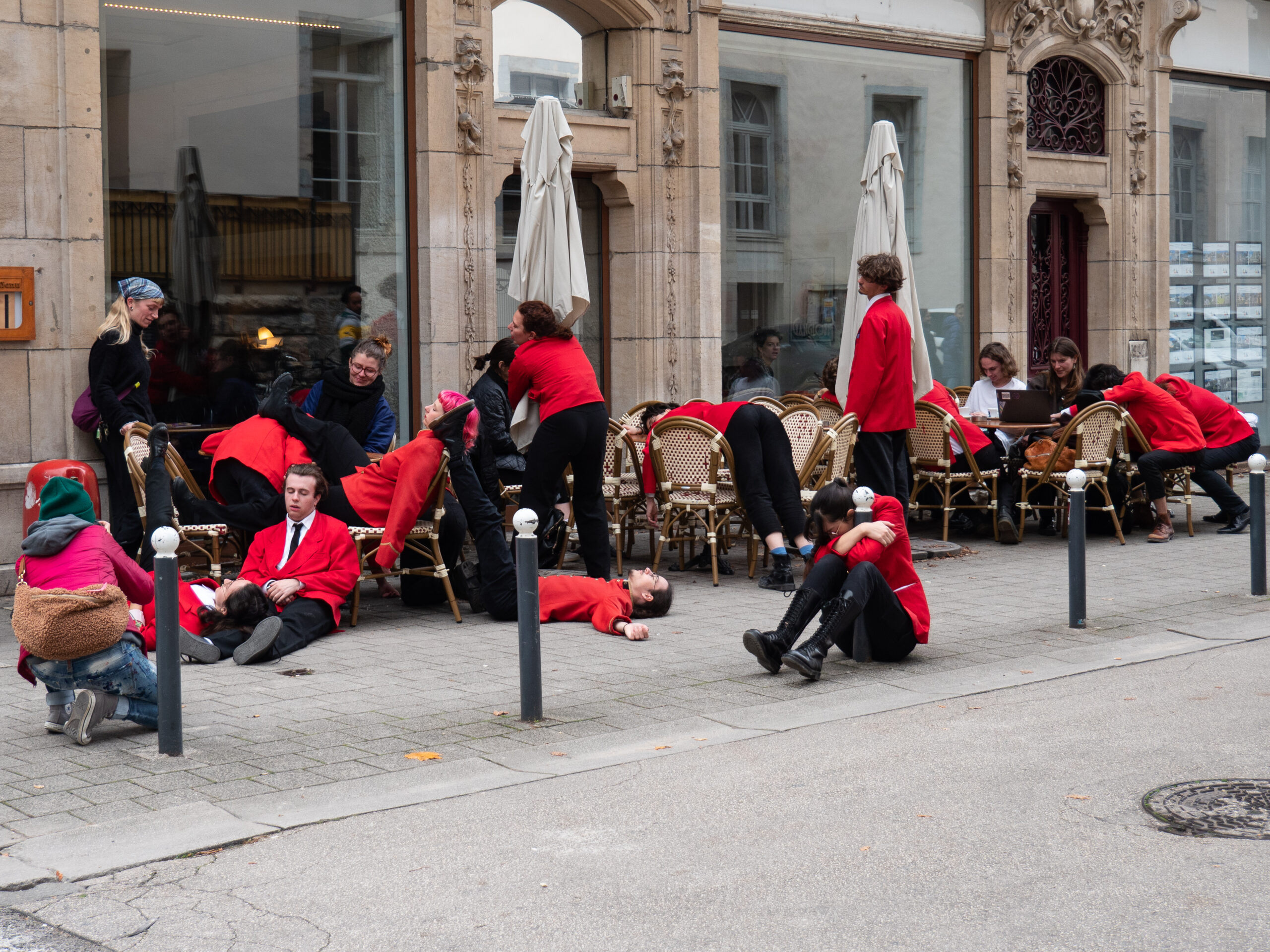 Les personnes vêtues de rouge installées à une terrasse, semblant s'être endormies sur les chaises, les tables, le sol, les poteaux du trottoir