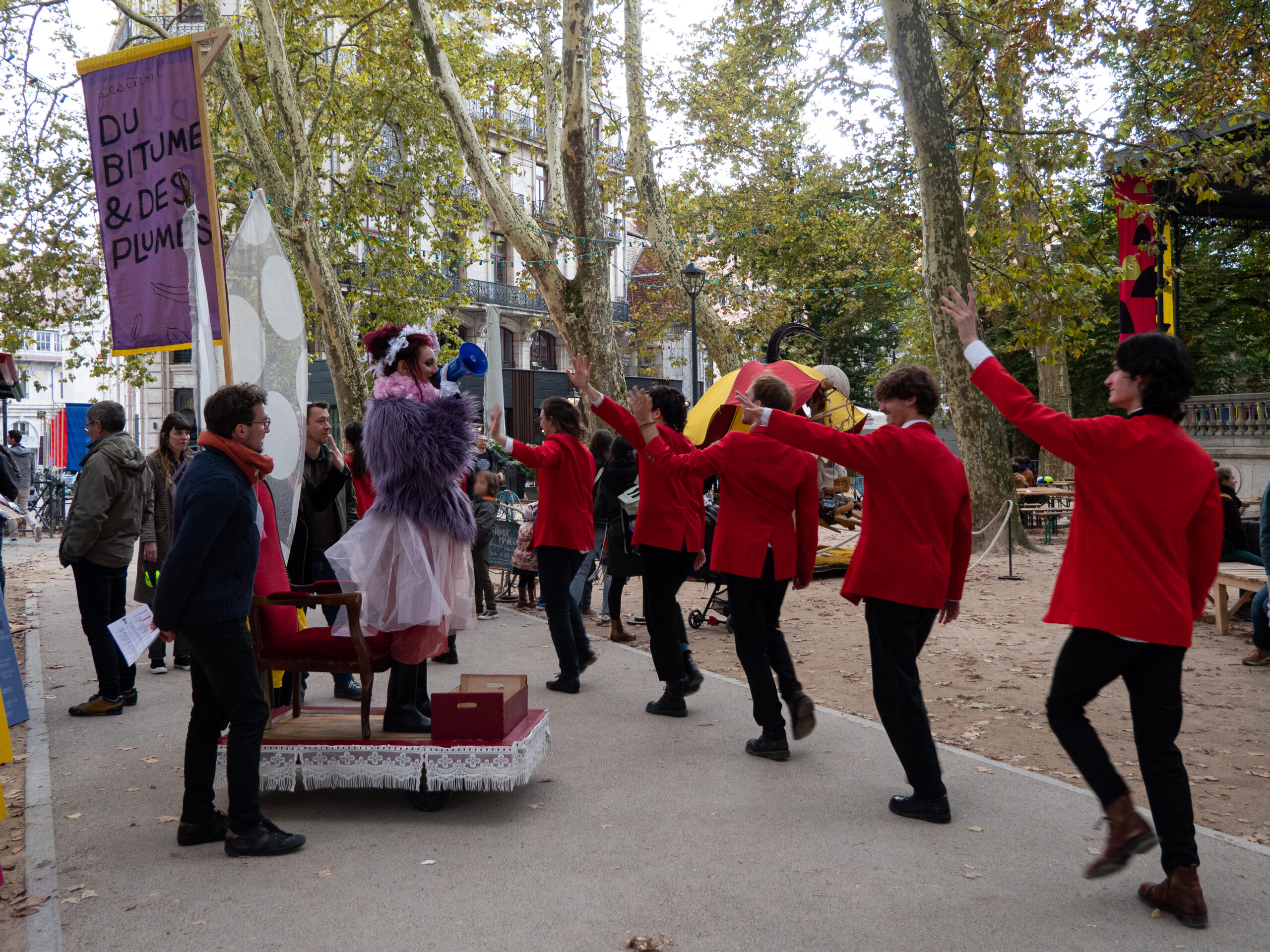 Défilé de cinq personnes vêtues de rouge devant un char constitué d'un fauteuil Louis 14 rouge sur lequel se trouve une femme habillée d'un haut en poils et d'une jupe tutu, tenant un mégaphone