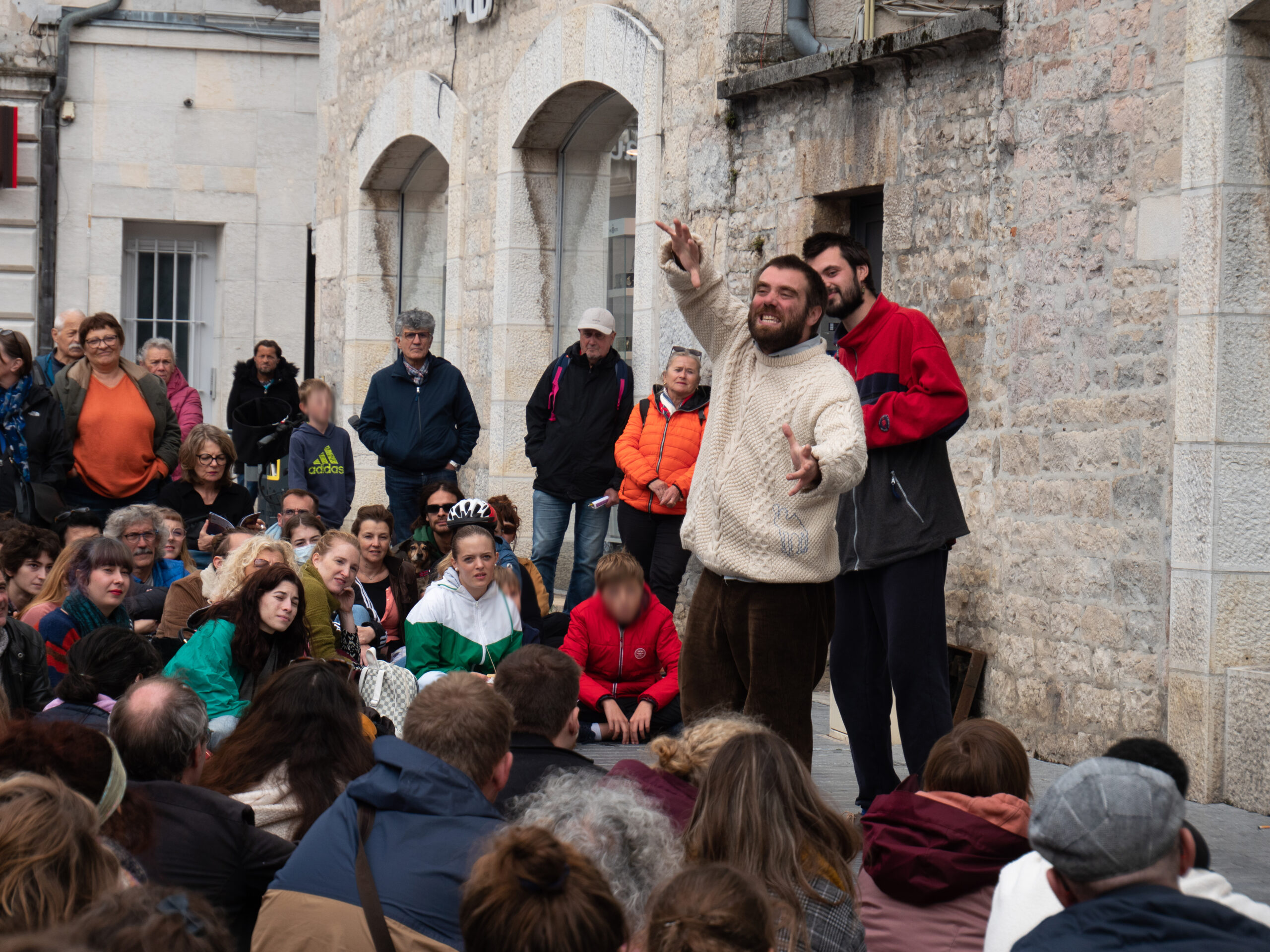 Foule de personnes assises devant un showman contre le mur, place Pasteur