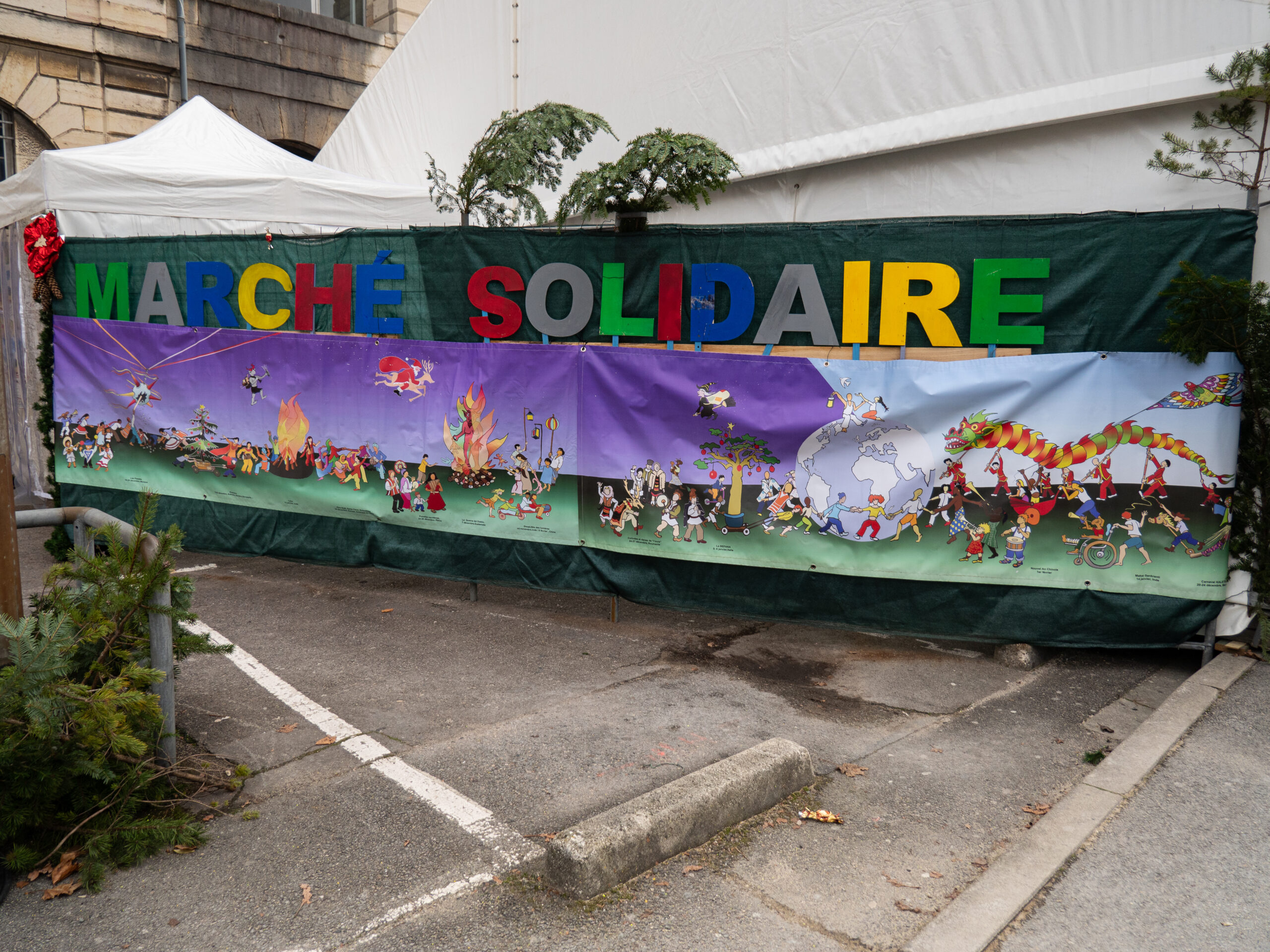 L'inscription Marché Solidaire en lettres colorées, en-dessous de laquelle une banderole représente des personnes de toutes cultures célébrant diversement les fêtes de fin d'années