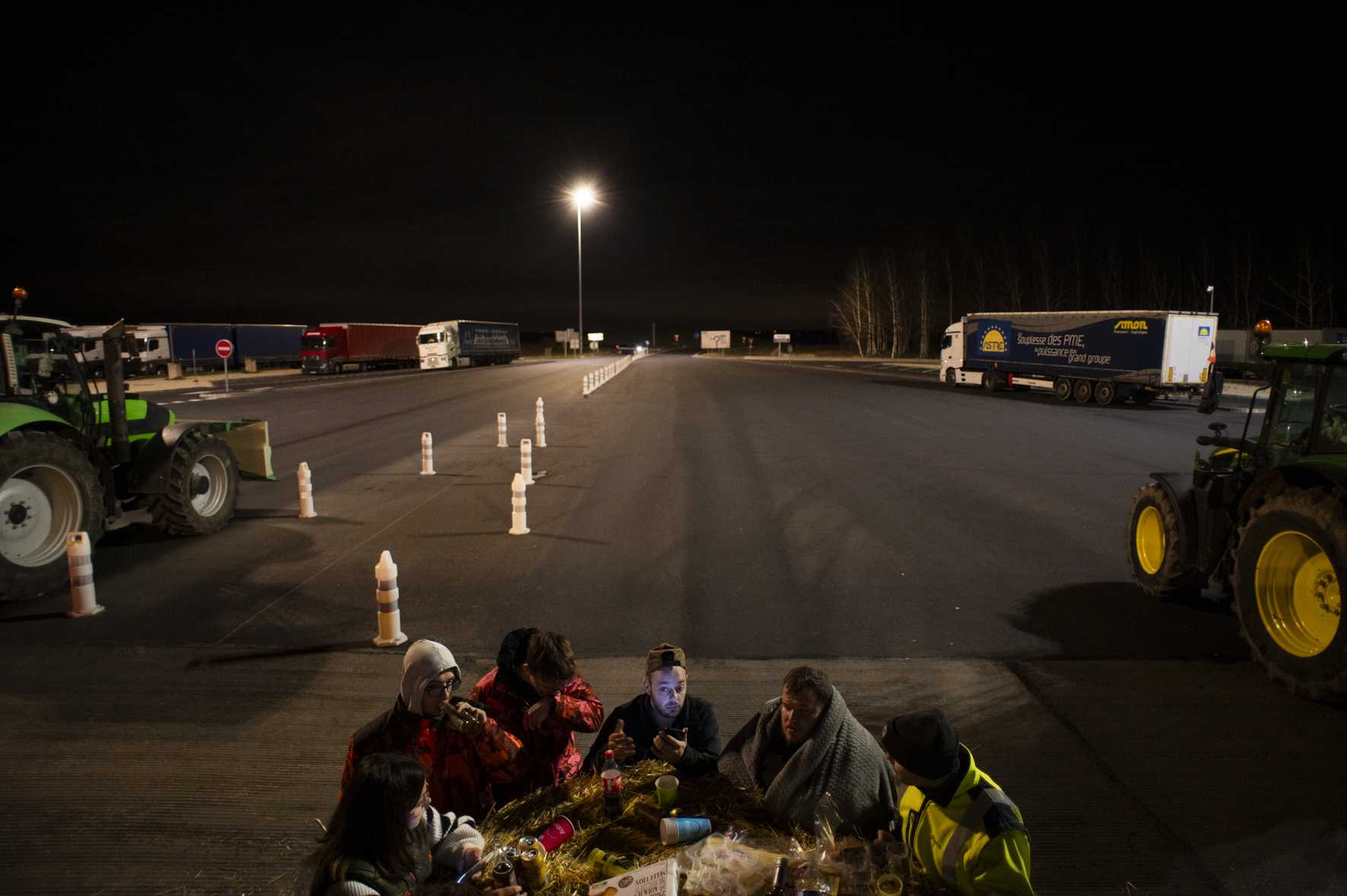 photo de nuit, pique-nique improvisé sur un péage autoroutier, au milieu des tracteurs, par cinq personnes chaudement vêtues