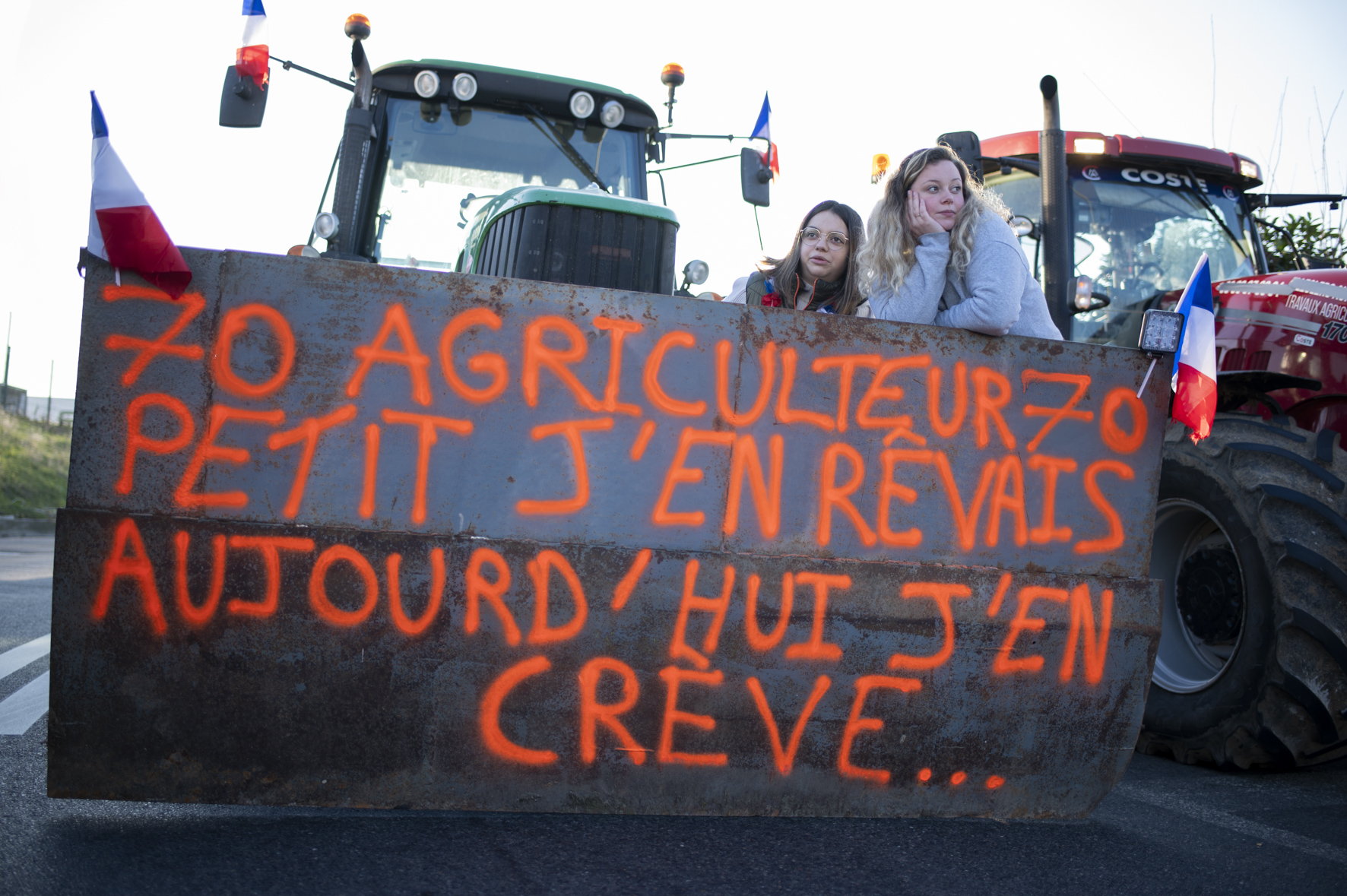 deux jeunes femmes au-dessus de deux plaques de métal déployées sur un tracteur, sur laquelle on peut lire : agriculteur petit j'en rêvais, aujourd'hui j'en crève.