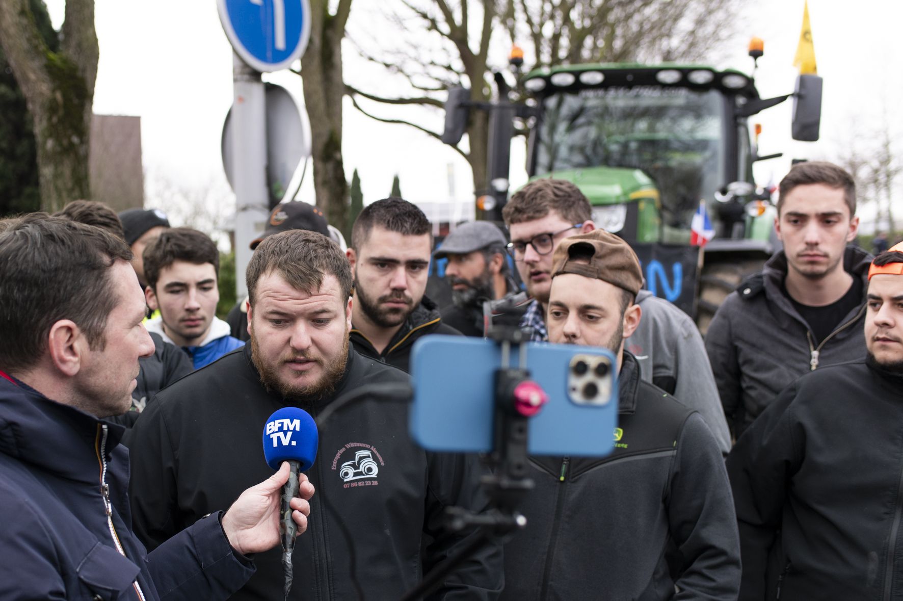 Un groupe d'agriculteurs en train de répondre à une interview de BMF TV, sur fond de tracteur bloquant la route