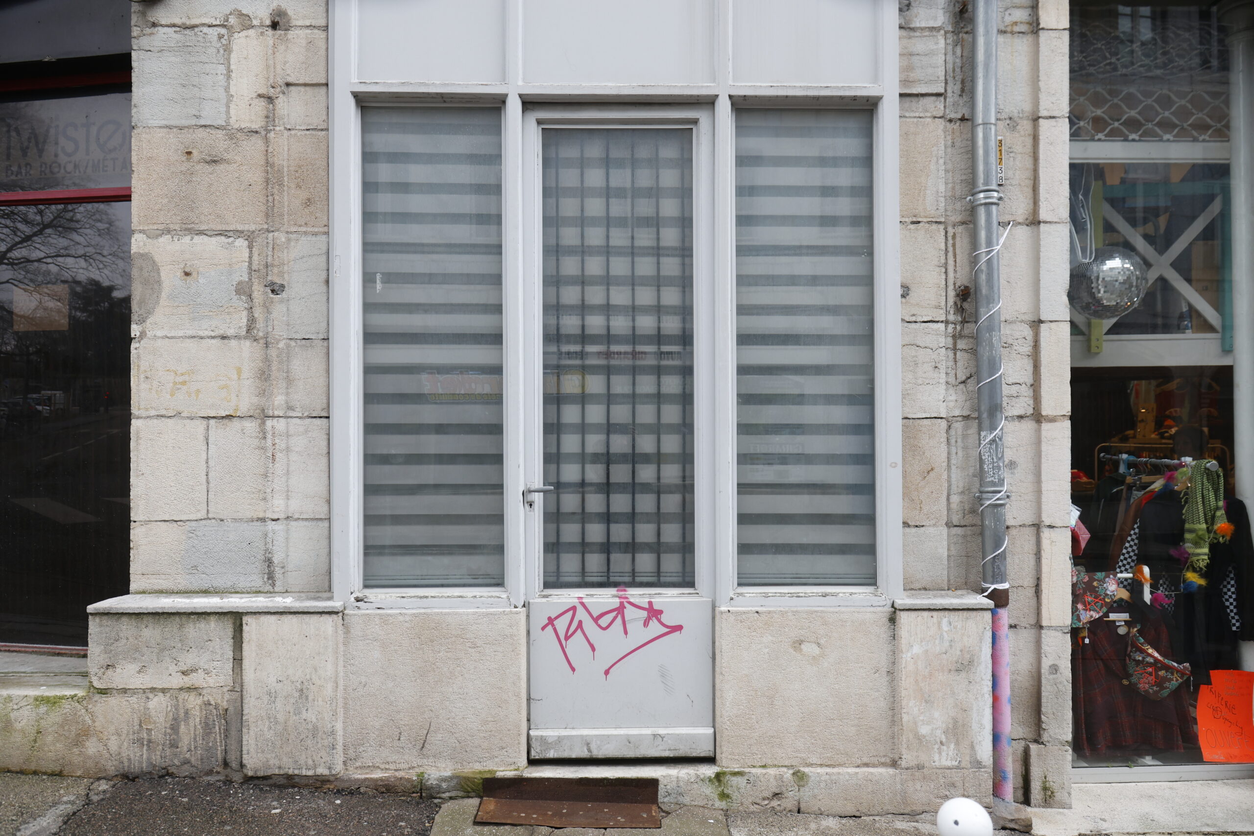 Photo de la devanture d'un magasin inconnu, fermé, porte et vitrine opacifiée, avec un tag sur la porte blanche