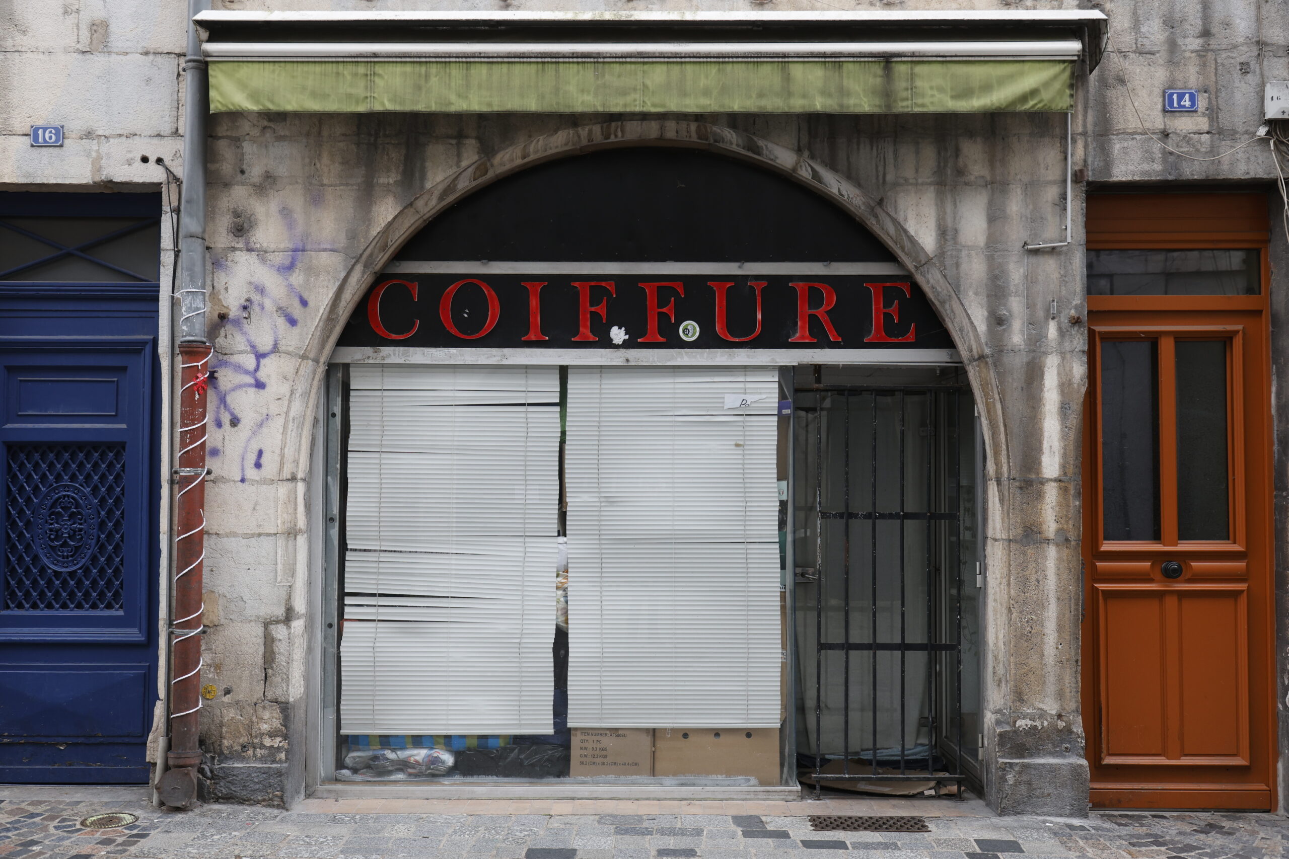 Photo de la devanture d'un salon de coiffure, fermé, la vitrine sous l'arche en pierre entièrement obstruée