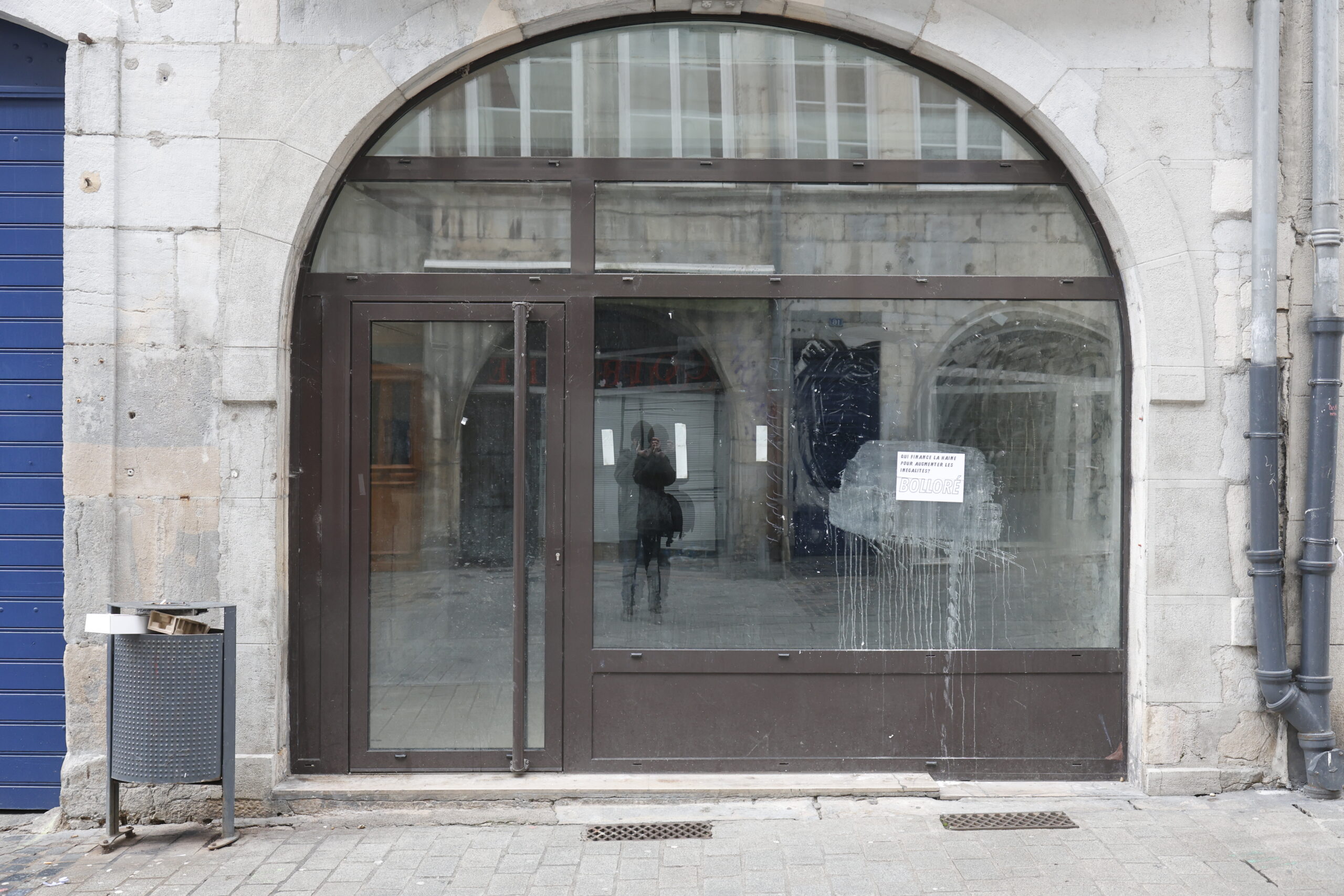 Photo de la devanture d'un commerce inconnu, fermé, la vitrine et la porte à montants marrons laissée vides.