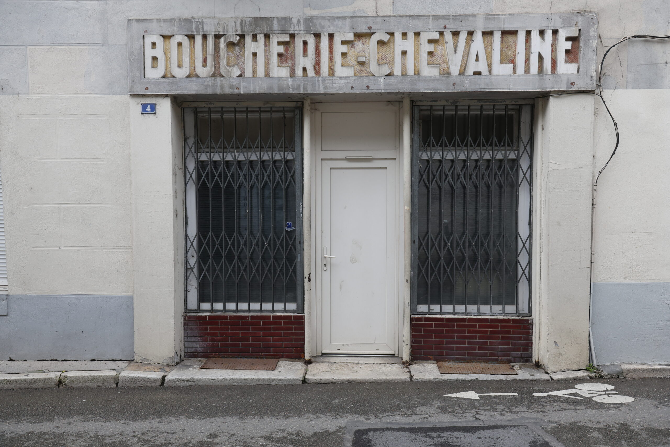 Photo de la devanture d'une boucherie chevaline fermée, la double vitrine barrée de rideaux de fer