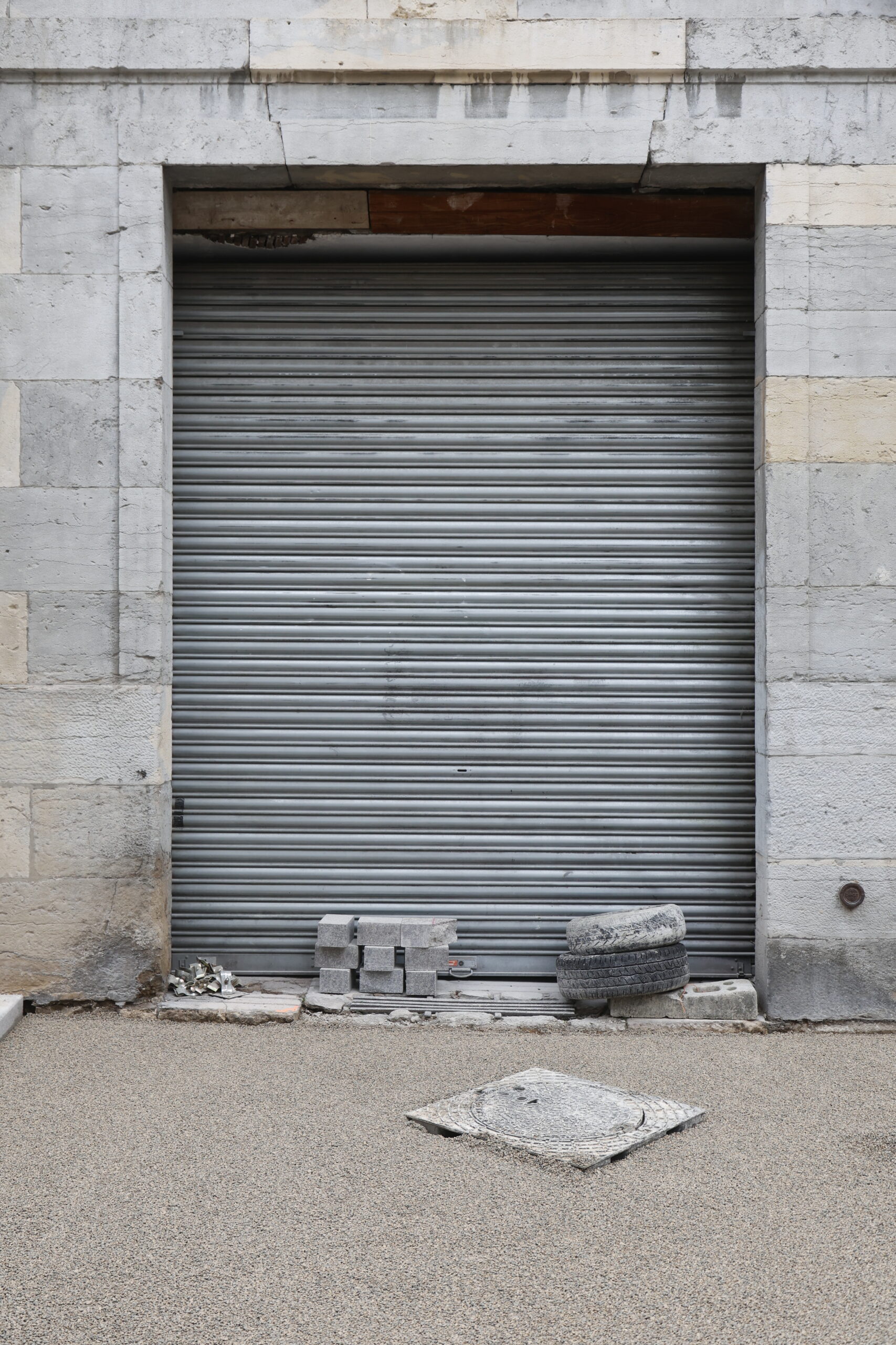 Photo de la devanture de magasin inconnu, volet en fer entièrement tiré, avec deux pneus et des pavés empilés sur le pas de porte