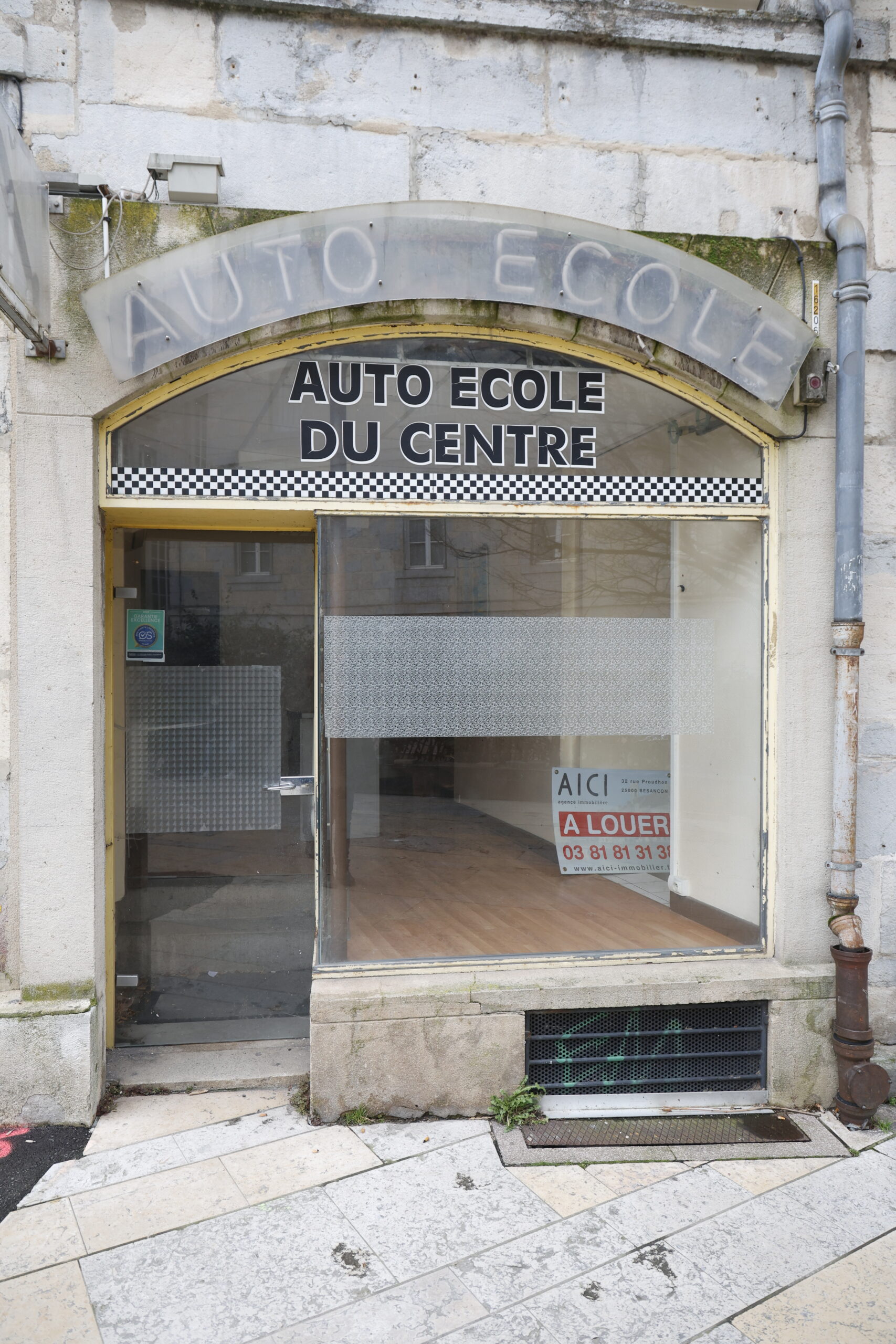 Photo de la devanture de l'auto-école du centre, fermée, locaux vide et panneau "à louer" sur la vitrine