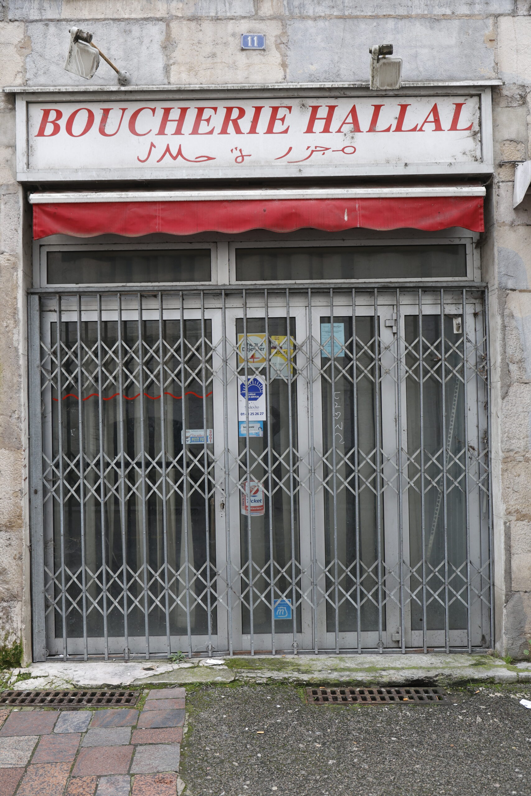 Photo de la devanture d'une boucherie hallal, fermée, le rideau de fer entièrement tirée et la vitrine opacifiée