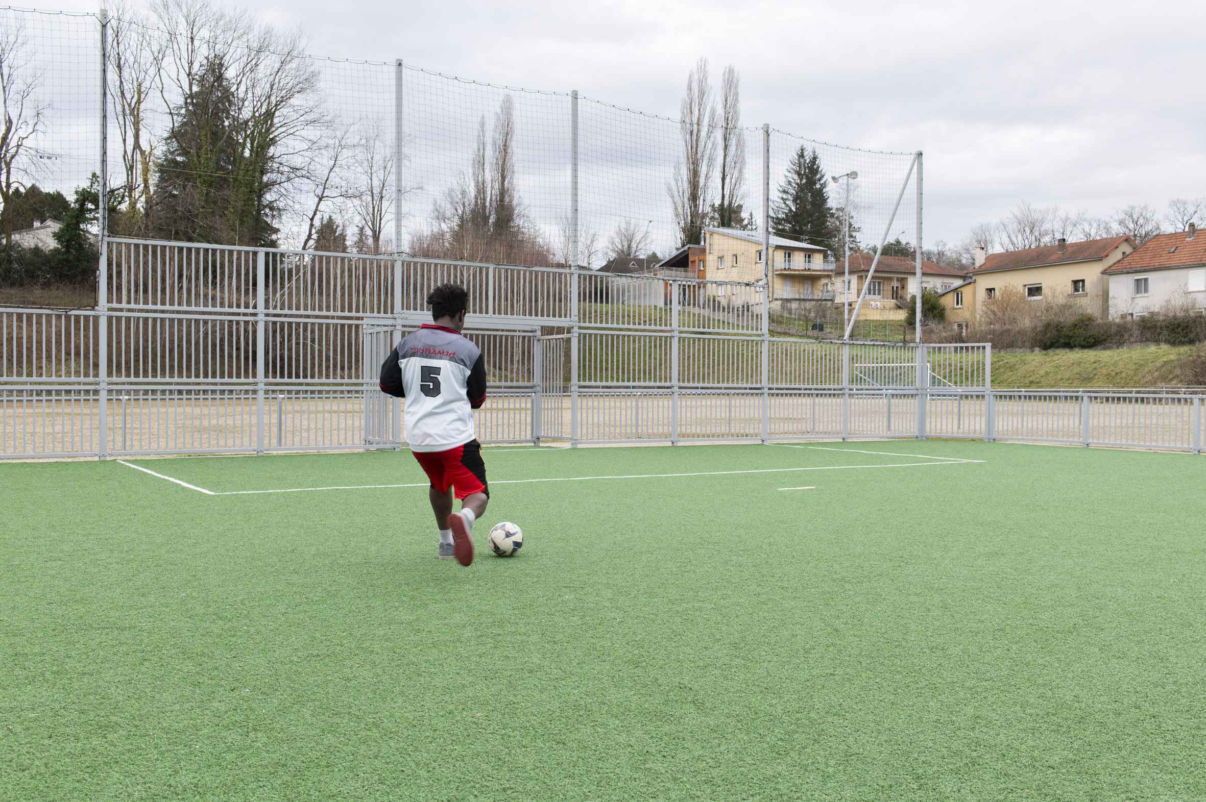 Une jeune homme jouant au foot sur un stade synthétique